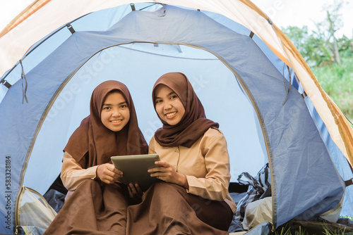 two girl scouts in veil smiling using tablet in tent in nature