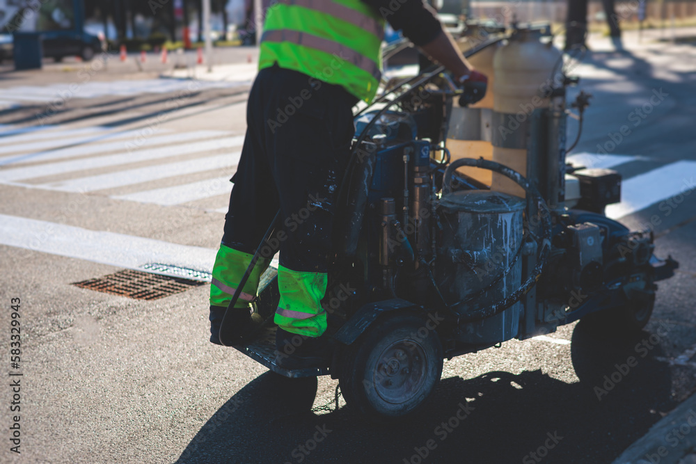 Obraz premium Process of making new road surface markings with a line striping machine, workers improve city infrastructure, demarcation marking of pedestrian crossing with a hot melted paint on asphalt pavement
