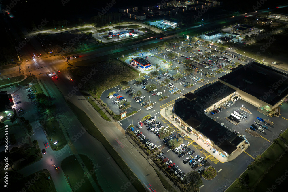 Aerial night view of many cars parked on parking lot with lines and markings for parking places and directions. Place for vehicles in front of a grocery mall store
