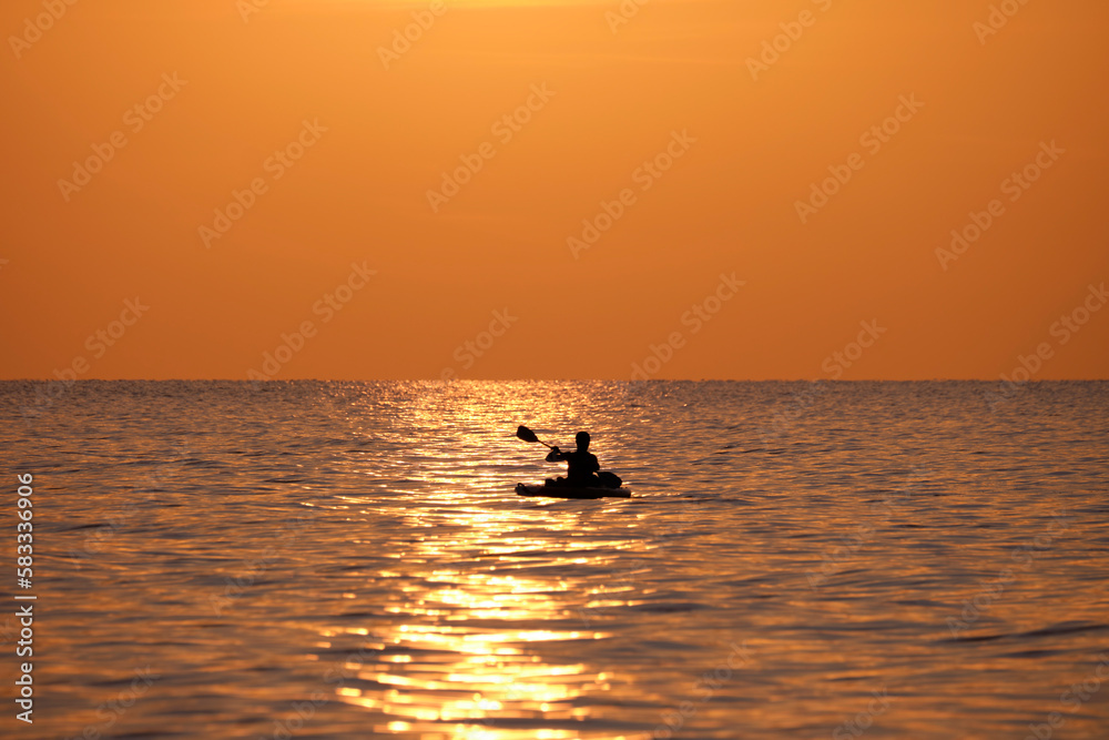 Dark figure of sportsman rowing alone on his kayak boat on sea water at sunset. Active extreme sports concept