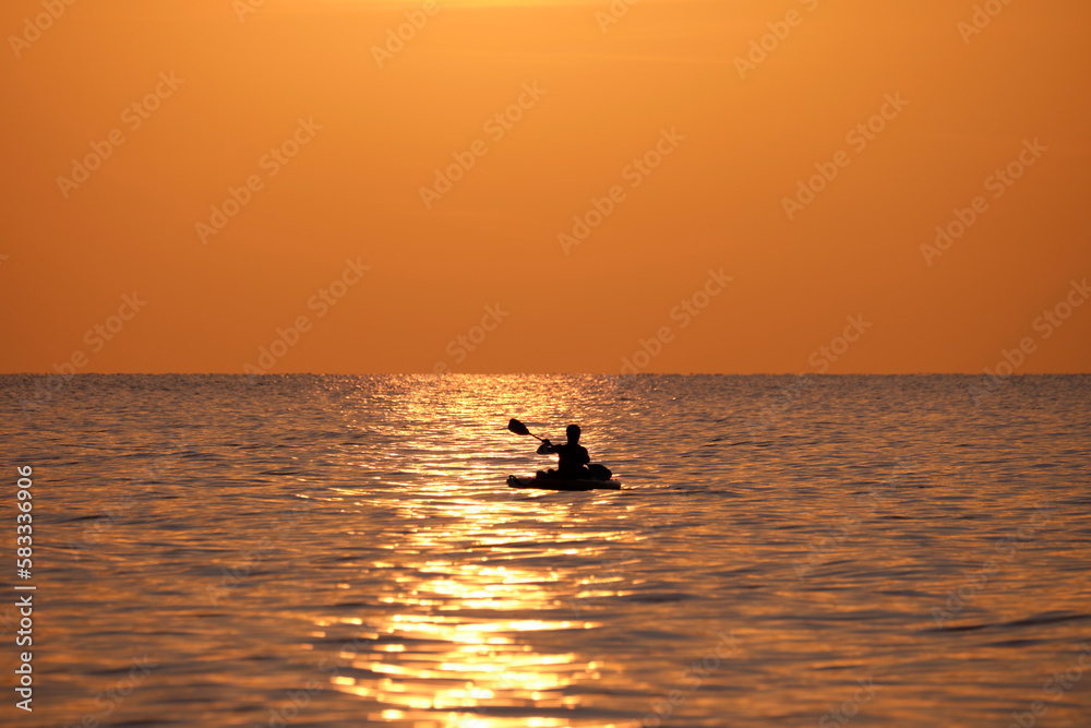 Fototapeta premium Dark figure of sportsman rowing alone on his kayak boat on sea water at sunset. Active extreme sports concept