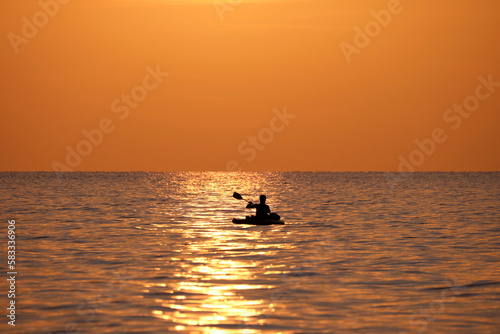 Dark figure of sportsman rowing alone on his kayak boat on sea water at sunset. Active extreme sports concept
