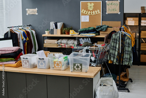 Fotografie Row of plastic garbage bins with recycle symbol standing on desk against racks w