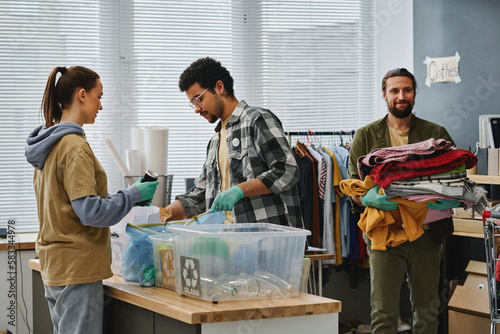 Принти на полотні Two young volunteers sorting garbage while man carrying stack of second hand clo
