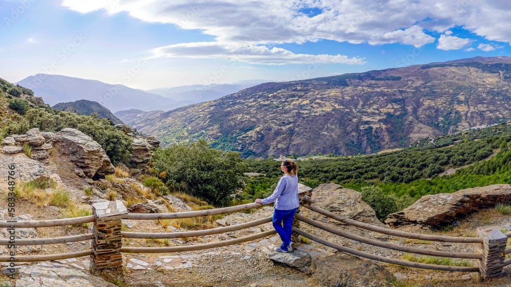 Pretty young woman dressed in jeans and sweatshirt enjoying the landscape of a valley in the Alpujarra of Granada