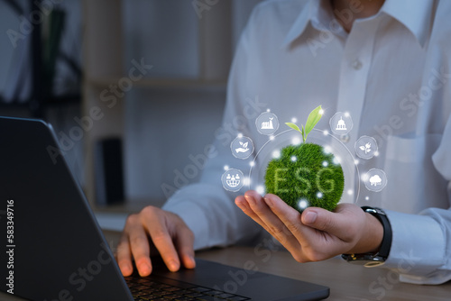 Businessmen use a computer to analyze ESG, and holding Green ball that writes the word with ESG icons. ESG environmental social governance business strategy investing concept.