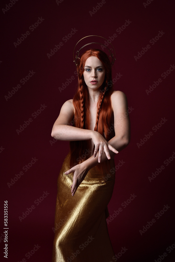 Close up fantasy portrait of beautiful woman model with red hair, goddess silk robes & gold crown. Posing with gestural hands reaching out, isolated on dark red studio background Close up fantasy portrait of beautiful woman model with red hair, goddess silk robes & gold crown. Posing with gestural hands reaching out, isolated on dark red studio background