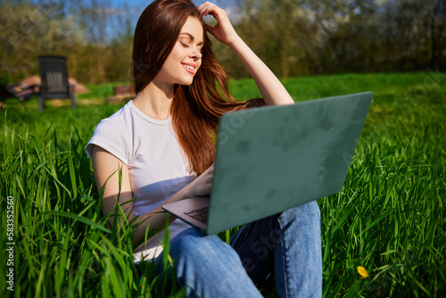 happy, joyful woman working on a laptop while sitting in a field photo