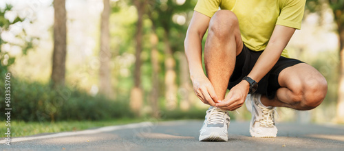 Young athlete man tying running shoes in the park outdoor, male runner ready for jogging on the road outside, asian Fitness walking and exercise on footpath in morning. wellness and sport concepts