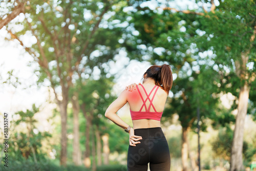 Young fitness woman holding her sports injury shoulder and neck, muscle painful during training. Asian runner female having body problem after exercise outside in summer