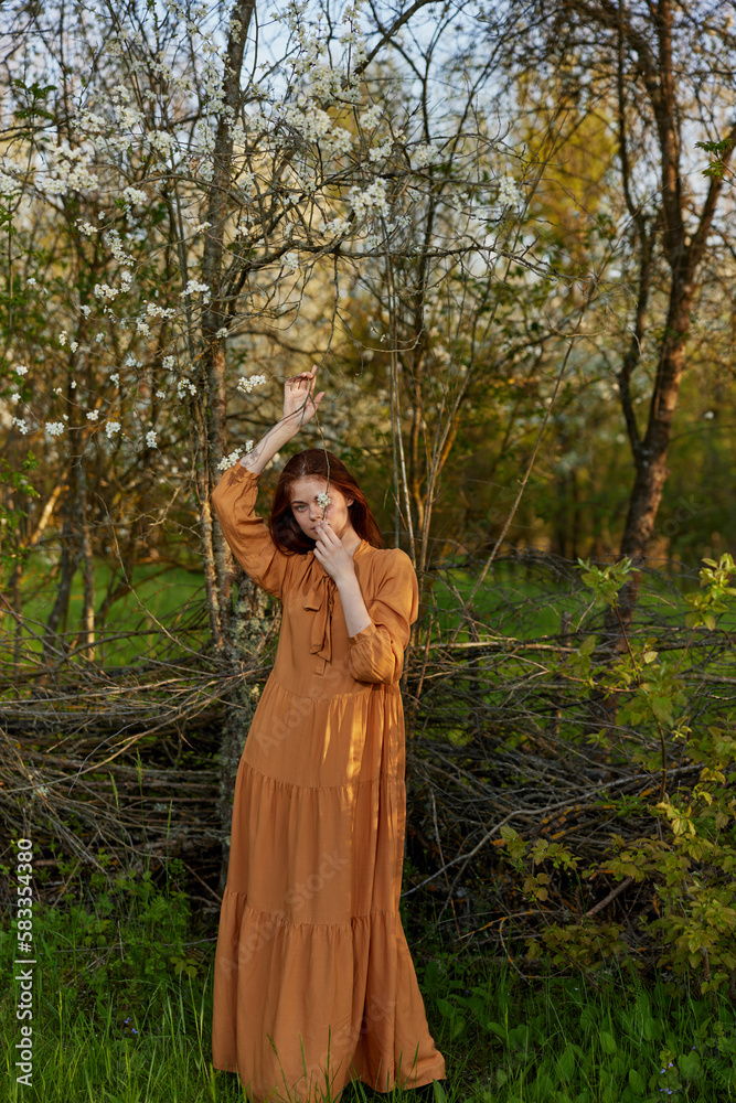 an elegant, sophisticated woman poses standing near a wicker fence at the dacha in a long orange dress an elegant, sophisticated woman poses standing near a wicker fence at the dacha in a long orange dress