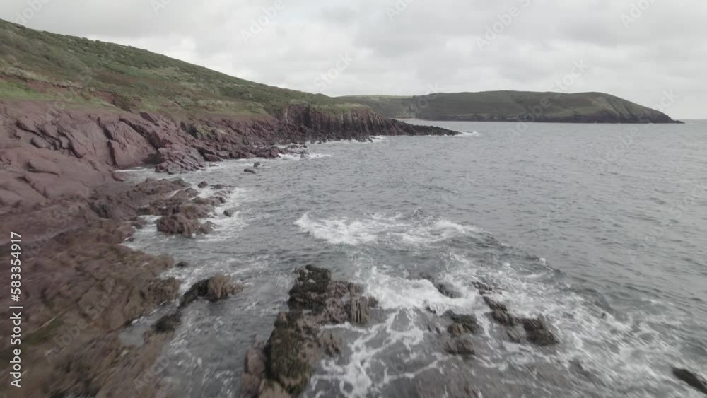  Rocky beach on sea coast. Low flights above waves washing stones on cloudy day. Blue Water, South Wales, UK