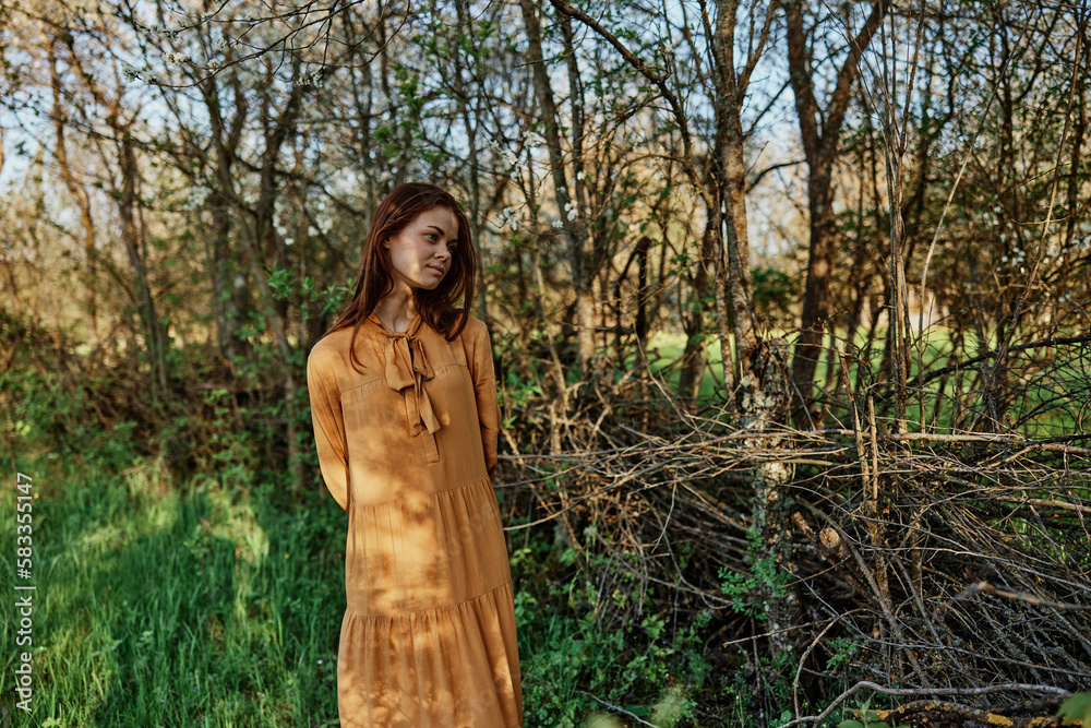 a beautiful, slender woman with long hair walks in the shade near the trees, dressed in a long orange dress, enjoying the weather and the weekend a beautiful, slender woman with long hair walks in the shade near the trees, dressed in a long orange dress, enjoying the weather and the weekend