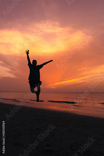 Silueta de persona saltando con los brazos abiertos en la playa durante el atardecer