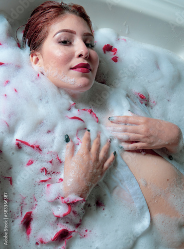 beautiful red-haired woman, with a beautiful look celebrating love with rose petals in the bathtub, woman in the tub with foam and rose petals, red lips like crimson, semi-naked woman in the jacuzzi