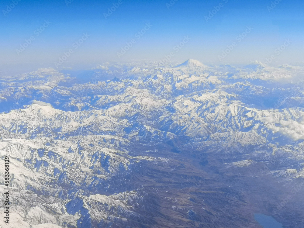 Snowy mountains with clouds as background. View from the airplane window.