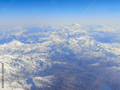 Snowy mountains with clouds as background. View from the airplane window. © schankz