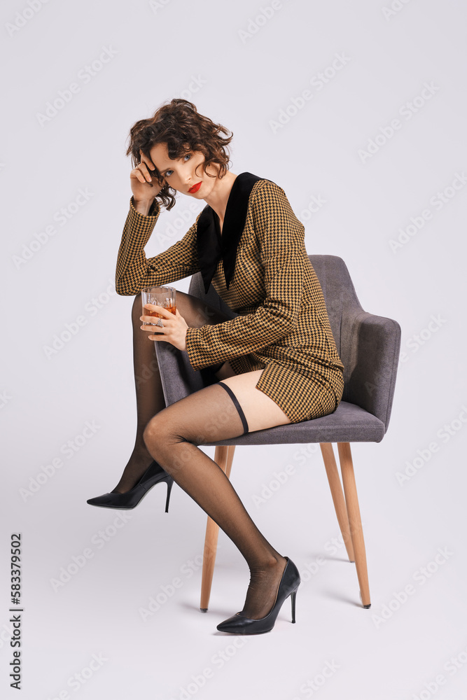 Woman with glass of whiskey threw one leg on armrest of chair Woman with glass of whiskey threw one leg on armrest of chair