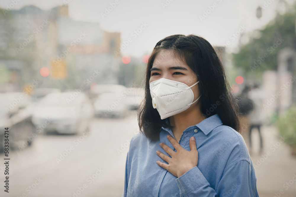 Asian woman wearing the N95 Respiratory Protection Mask against PM2.5 air pollution and headache Suffocate. City air pollution concept Asian woman wearing the N95 Respiratory Protection Mask against PM2.5 air pollution and headache Suffocate. City air pollution concept