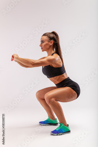 beautiful fitness woman in sportswear squatting and doing squats in the gym on a gray background.
