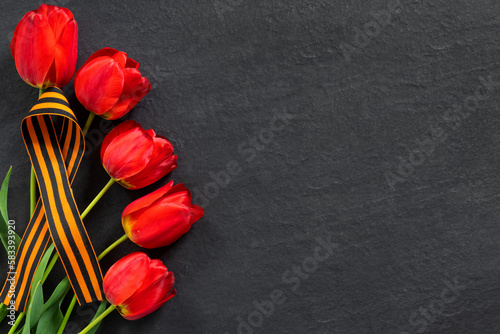 Happy Victory Day! May 9 Russian Victory Day. St. George ribbon with bouquet of red tulips on  black granite monument with empty space for text. photo