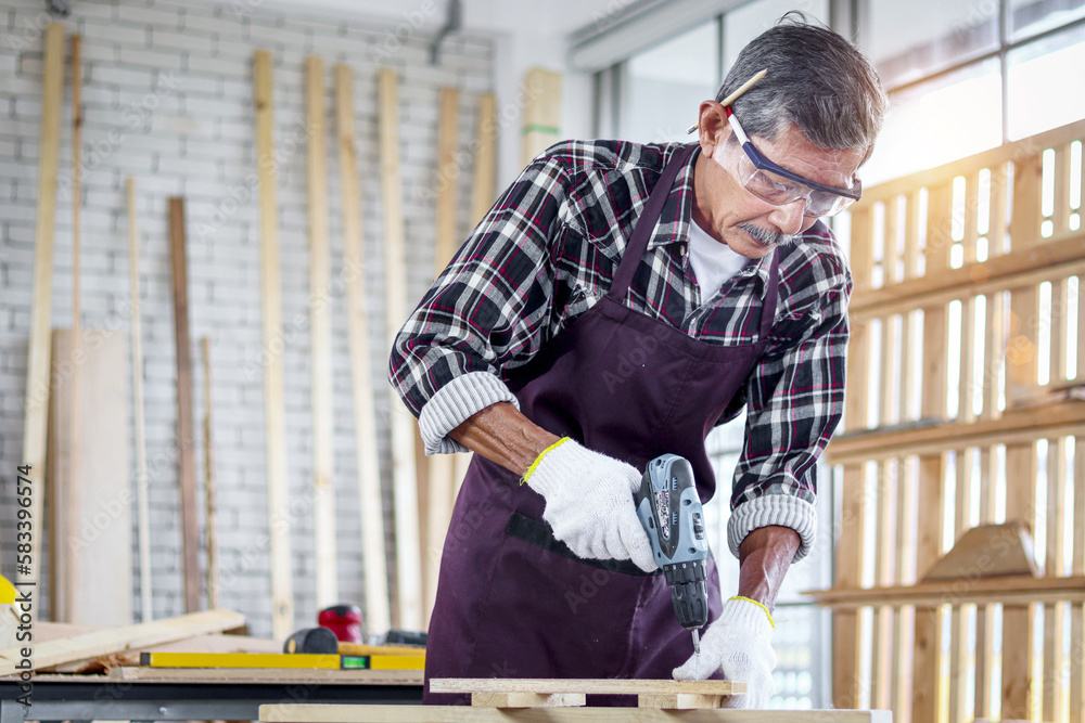 Senior Asian carpenter wear safety glasses and cloth gloves in woodwork workshop, old citizen craftsman work with hand drill in joinery carpentry, cheerful elderly grandpa enjoy DIY hobby Senior Asian carpenter wear safety glasses and cloth gloves in woodwork workshop, old citizen craftsman work with hand drill in joinery carpentry, cheerful elderly grandpa enjoy DIY hobby