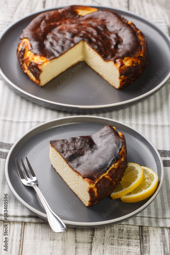Fototapeta premium Sliced tender creamy burnt basque cheesecake with lemon wedges close-up on a plate on the table. Vertical