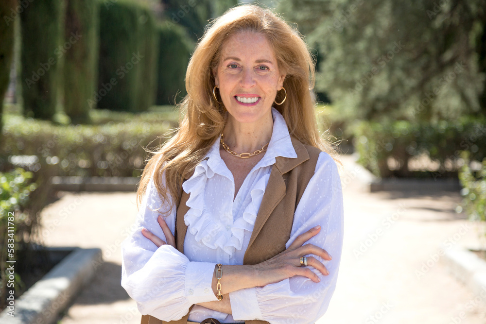 middle-aged woman smiling looking at camera with her arms crossed in park middle-aged woman smiling looking at camera with her arms crossed in park
