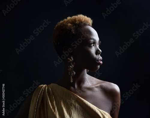  fantasy portrait of beautiful african woman model with afro, goddess silk robes and ornate floral wreath crown. gestural Posing holding golden flowers. isolated on dark studio background 