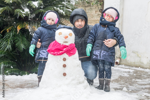 Ritratto di un giovane padre con le figlie gemelle d'inverno con un pupazzo di neve. photo