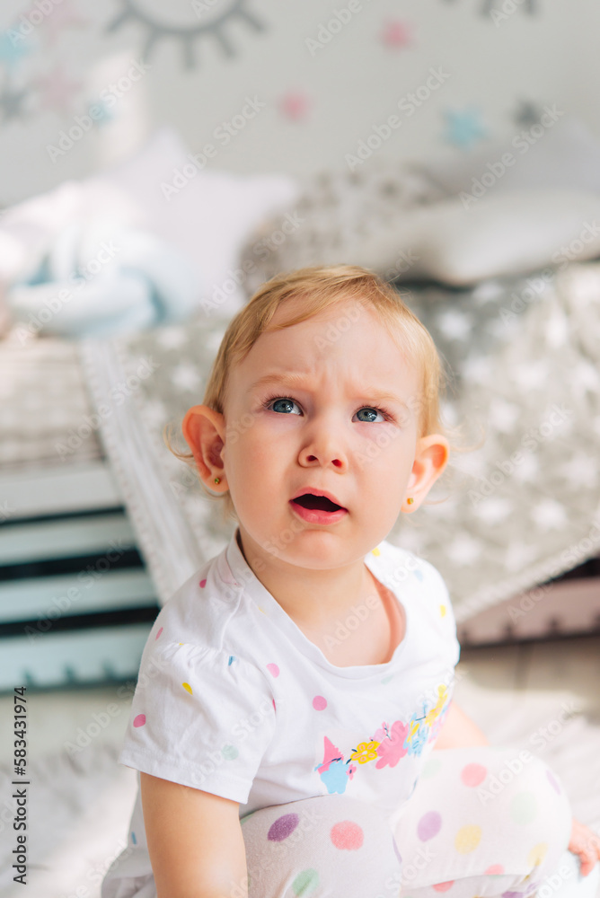 Fototapeta premium little cute healthy girl toddler in a white t-shirt made of natural fabric, looking at the camera, the baby is at home