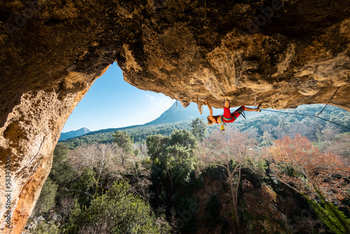 A young rock climber on an overhanging cliff. The climber climbs the rock. The girl is engaged in sports climbing.