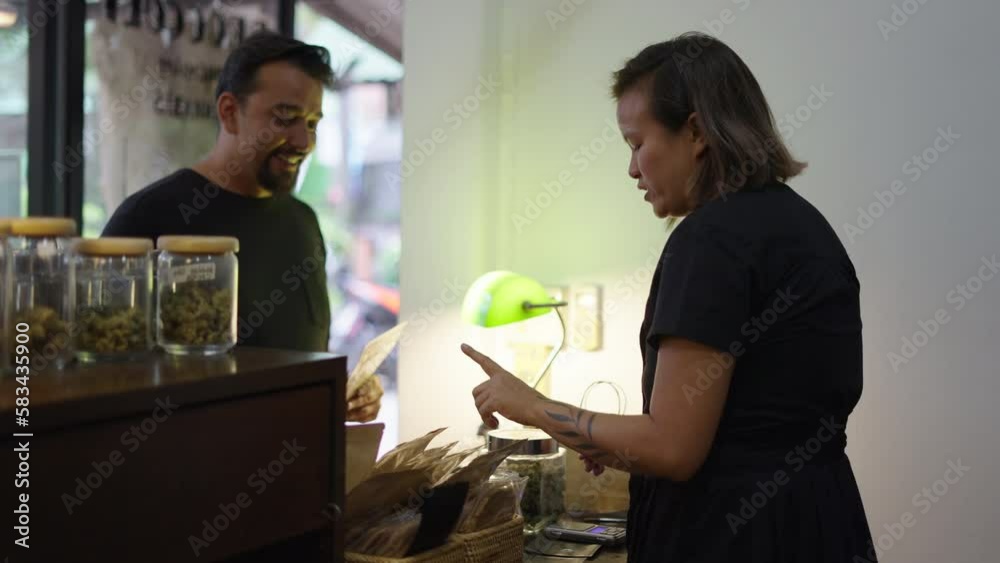 Asian retailer woman helping to the client to choose marihuana product in a dispensary Asian retailer woman helping to the client to choose marihuana product in a dispensary