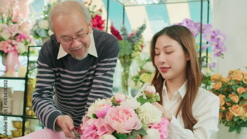 Asian young beautiful female florist worker and senior man shop owner arranging blossoms bouquet together in valentine, happy work with smile and cheerful in colorful flower store, SME entrepreneur. 