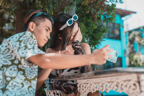 A young woman covers her face, refusing to take a picture with her boyfriend. Embarrassed and ashamed to be seen with her date.