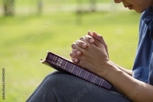 Man's hands pray over a bible in a field during beautiful sunlight in the morning. Hands folded to pray and seek the blessings of God, Holy Bible concept for faith, spirituality, worship, and religion