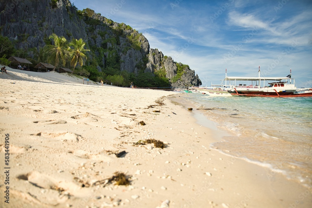 Paradise beach of Coron, Palawan in the Philippines with fine white beach, palm trees, majestic rocks and a boat in the water.