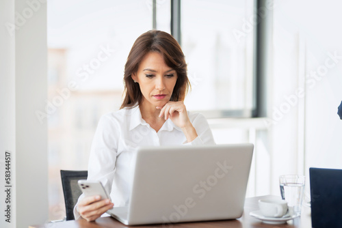 Portrait of confident business woman wearing white shirt and using laptop while working at the office