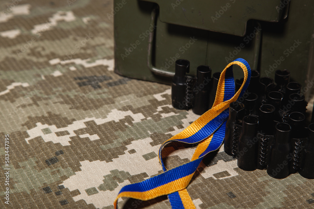 Fototapeta premium Military green box, machine gun ribbon and blue-yellow ribbon, colors of the Ukrainian flag, on the background of the green military pixel.