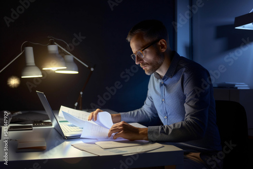 A man sits at a desk in a dark room, reading a documents Generative AI photo