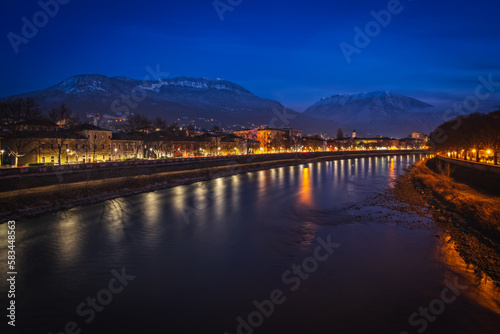 Night view of the city of Trento, Italy with snow capped mountain in background. Night view of a city between mountains and river Adige. Long exposure picture taken in January 2023