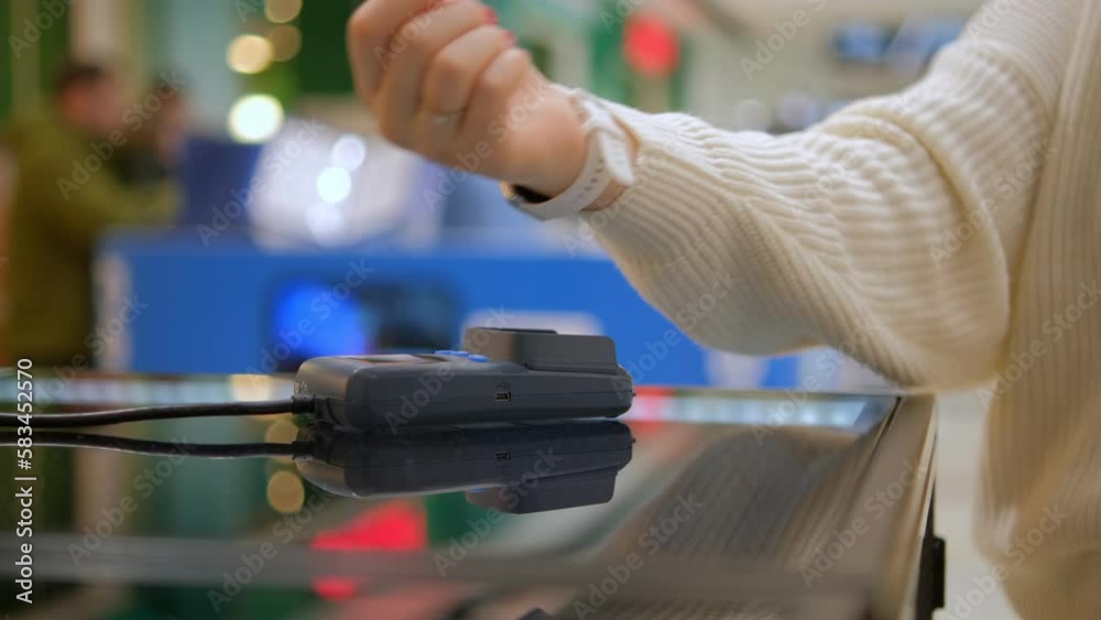 Wireless payment by smart watch using e wallet on pos terminal or card reader. Female buyer hand pays electronic cashless money at shopping place close up indoors Wireless payment by smart watch using e wallet on pos terminal or card reader. Female buyer hand pays electronic cashless money at shopping place close up indoors