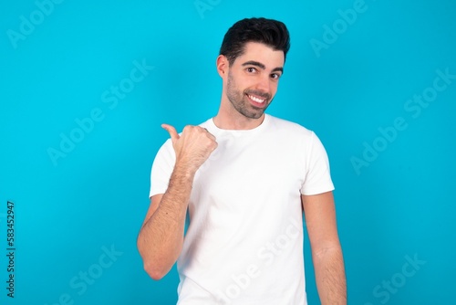Lovely Young man wearing white T-shirt over blue studio background pointing aside with forefinger, showing at copy space having news about bargains