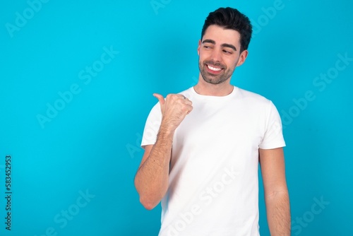 Charming Young man wearing white T-shirt over blue studio background looking at copy space having advertisements