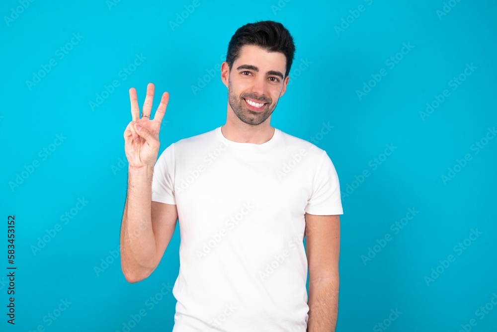Young man standing over blue studio background showing and pointing up with fingers number three while smiling confident and happy. Young man standing over blue studio background showing and pointing up with fingers number three while smiling confident and happy.