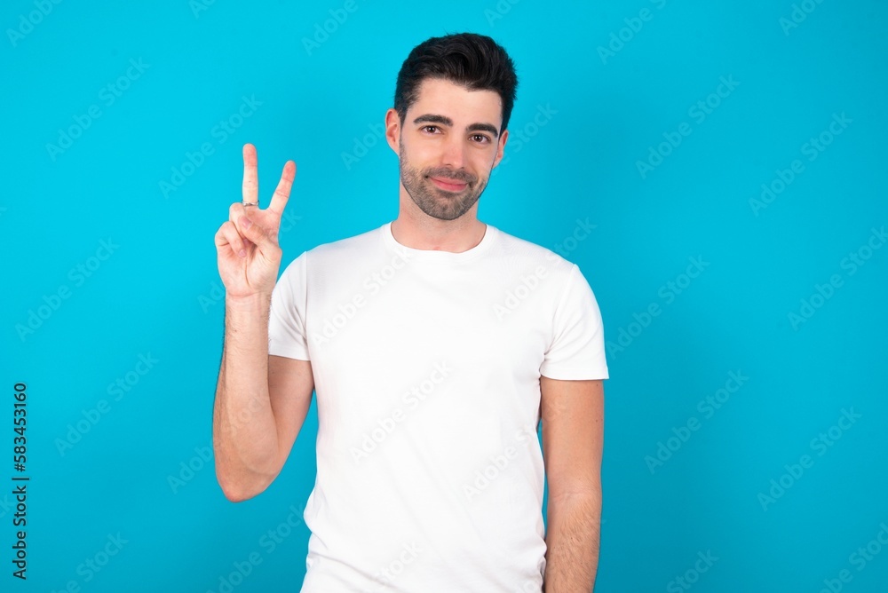 Young man standing over blue studio background showing and pointing up with fingers number two while smiling confident and happy. Young man standing over blue studio background showing and pointing up with fingers number two while smiling confident and happy.