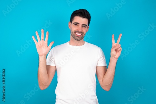 Young man standing over blue studio background showing and pointing up with fingers number seven while smiling confident and happy.