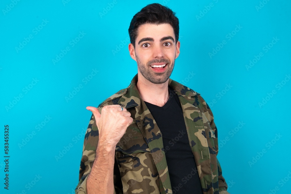 Impressed Young man standing over blue studio background point back empty space