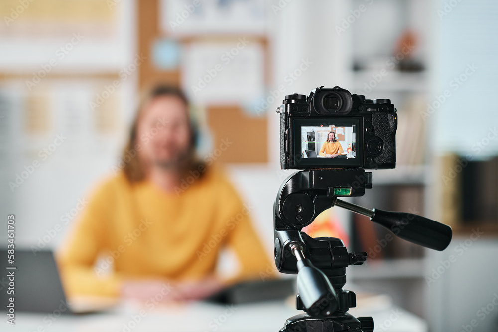 Mature man sitting at table in the classroom and recording lesson for his students on camera Mature man sitting at table in the classroom and recording lesson for his students on camera