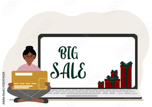 Online shopping. Big sale. A woman sits cross-legged in his hands holding a shopping card. Next to a laptop with gifts.